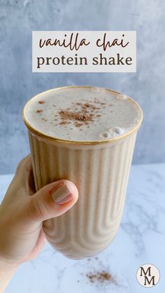 a hand holding up a cup filled with liquid on top of a marble countertop