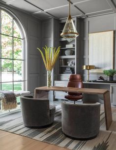 an elegant living room with large windows and modern furniture in the center, along with a wooden dining table surrounded by two swivel chairs