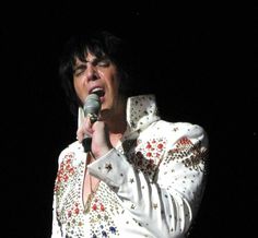 elvis presley singing into a microphone in his white suit with red and blue flowers on it