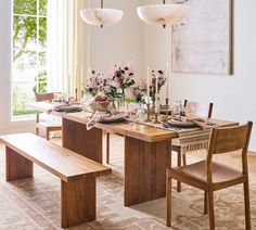 a dining room table set with place settings and flowers in vases on the table