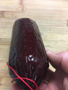 a hand holding a piece of chocolate covered in plastic wrap on top of a wooden table