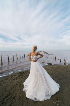 a woman standing on top of a beach next to the ocean wearing a wedding dress