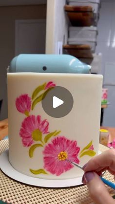 a person is using scissors to paint a flowered cup with flowers on the side