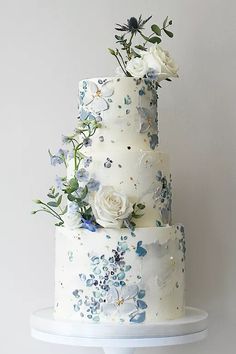 a three tiered white cake with blue and white flowers on the top, sitting on a stand