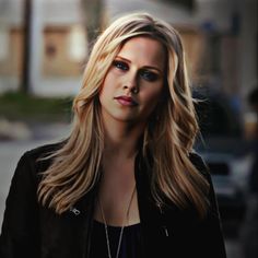 a woman with blonde hair and blue eyes is standing in front of a street corner