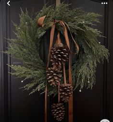 a wreath with pine cones and ribbons hanging from it's side on a door