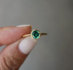 a woman's hand holding a ring with a green stone in the middle and gold band