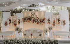 a decorated stage with couches, chairs and flowers on the wall behind it at a wedding