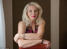 an older woman with her arms crossed leaning on a chair