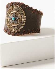 a brown leather cuff with a turquoise stone in the center on top of a white surface