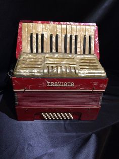 an old red and gold accordion sitting on a black cloth covered surface with its keys missing