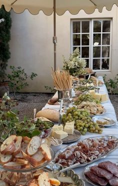 a table filled with lots of different types of food on plates and under an umbrella