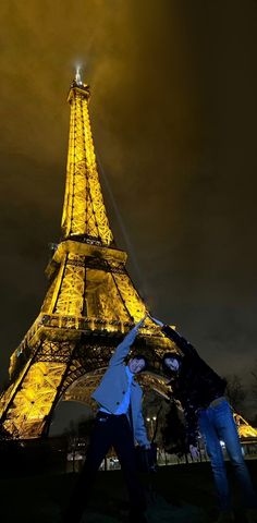 two people standing in front of the eiffel tower at night with their arms around each other