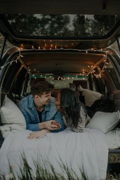 a man and woman laying in the back of a van with lights strung from it