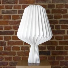 a white lamp sitting on top of a wooden table next to a brick wall and floor