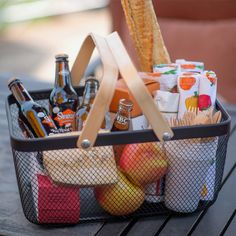 a picnic basket filled with beer, snacks and fruit on top of a wooden table