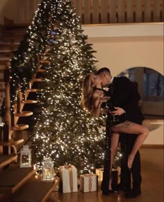 a man and woman kissing in front of a christmas tree