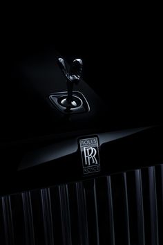 the hood ornament of a rolls royce logo on a shiny black car in the dark