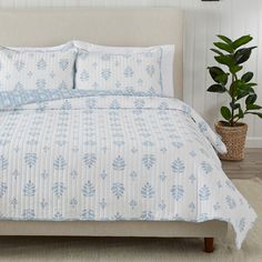 a bed with white and blue bedspread next to a potted plant