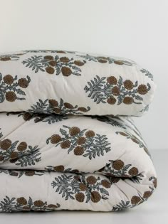 two pillows stacked on top of each other with pine cones and leaves printed on them