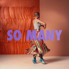 a woman is dancing with the words so many in front of her and an orange wall behind her