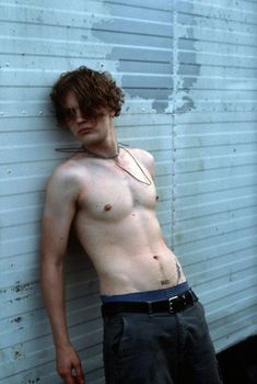 a shirtless young man leaning against a wall