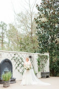 a bride standing in front of an outdoor fireplace with greenery on the wall behind her