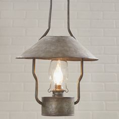 an old fashioned light hanging from a ceiling fixture with a brick wall in the background