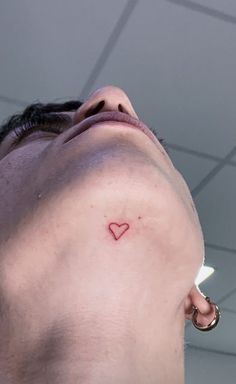 a man with a small heart tattoo on his left side behind his ear is looking up at the ceiling