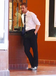 a man leaning against a wall wearing a tie