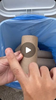 a person holding a roll of toilet paper in a blue trash can with the lid open