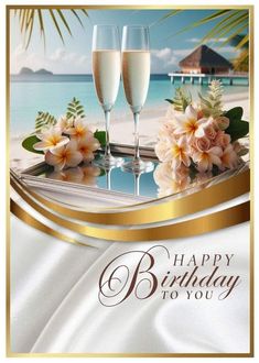 two glasses of champagne on a beach with flowers and palm trees in the background that says happy birthday to you