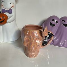 three ceramic halloween decorations are sitting on a white counter top, one has a skull and the other is a pumpkin