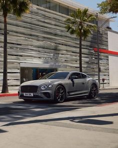 a grey sports car parked in front of a building with palm trees on the sidewalk