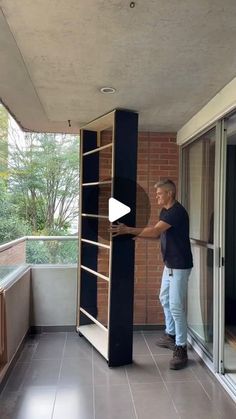 a man standing on top of a balcony next to an open door and holding onto a book shelf