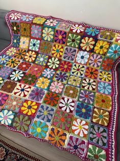 a multicolored granny afghan is displayed on a couch with a rug underneath it