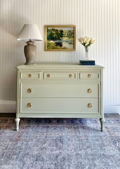 a white dresser sitting next to a lamp on top of a table