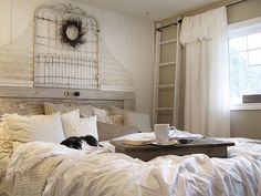 a white bed sitting under a window next to a table with a laptop on top of it