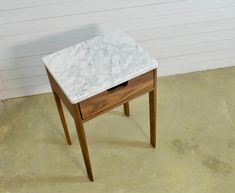 a white marble top end table with wooden legs on concrete floor next to brick wall