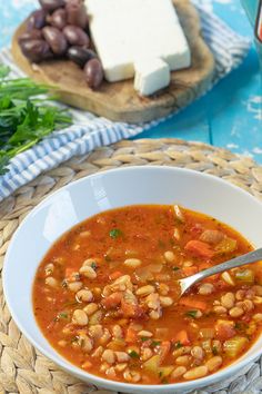 a white bowl filled with soup next to bread and vegetables on a blue table cloth