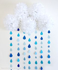 paper flowers and raindrops are hanging from the side of a white wall with blue drops