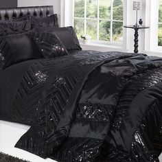 a black bed with sequins on it in front of a white wall and windows