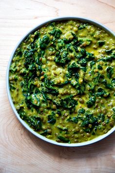 a white bowl filled with green food on top of a wooden table