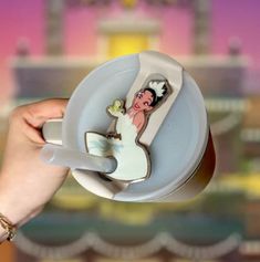 a person holding a coffee cup with a cake in the shape of a bride and groom on it