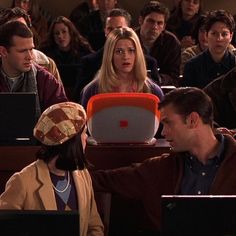 two people sitting in front of laptops with other people behind them looking at each other