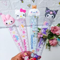 three hello kitty pencils are held up in front of a flower vase with pink roses