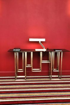 two metal tables against a red wall in a room with striped carpet and rug on the floor