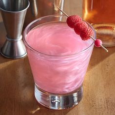 a pink drink with raspberries on the top and a cocktail shaker in the background