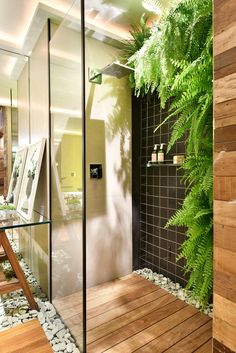 a bathroom with a wooden floor and green plants in the shower area, next to a glass wall