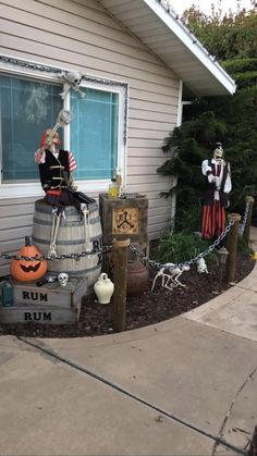 a house with halloween decorations on the front lawn and in front of it is a barrel full of pumpkins